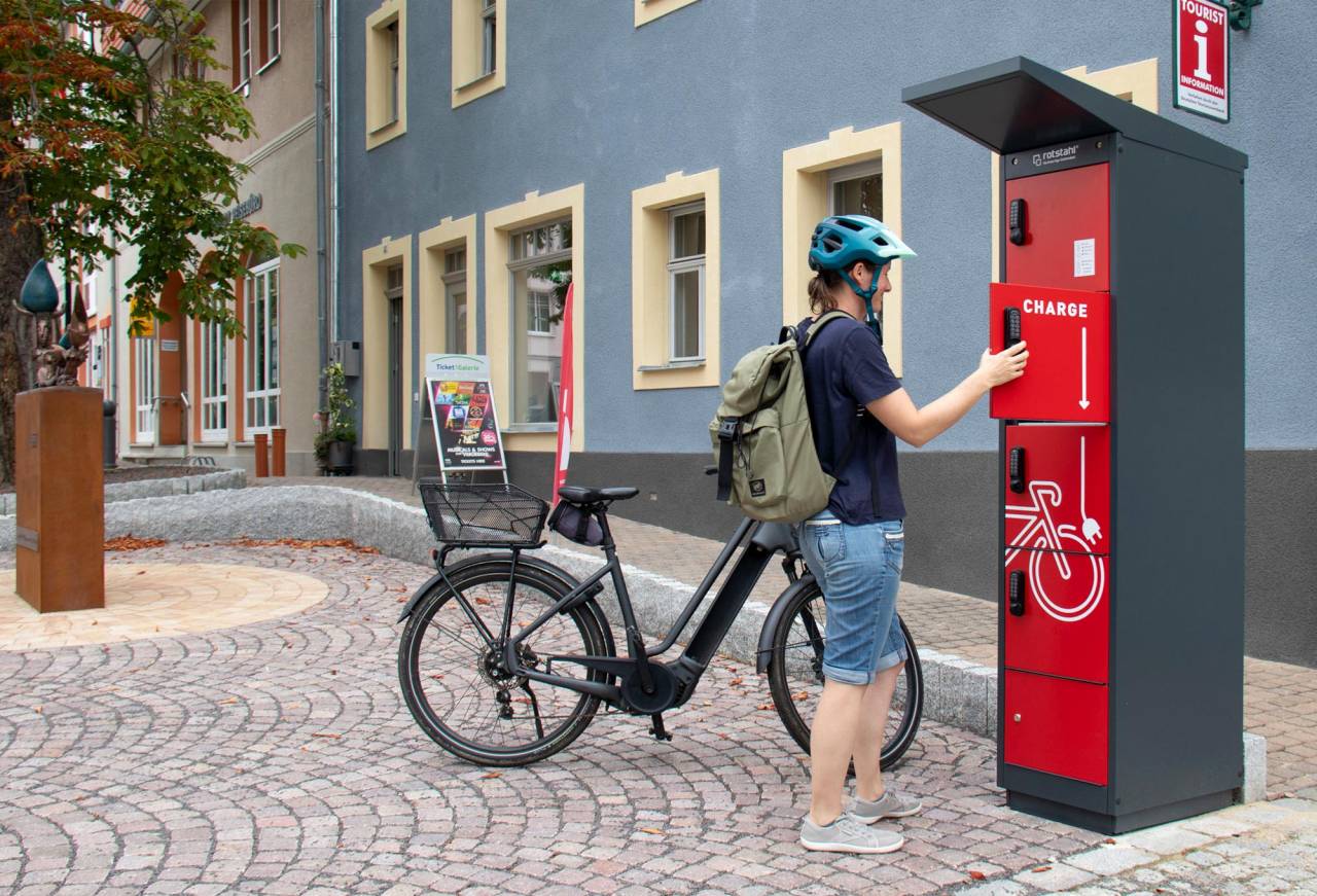 Mann mit Fahrrad an einer roten E-Bike Ladestation