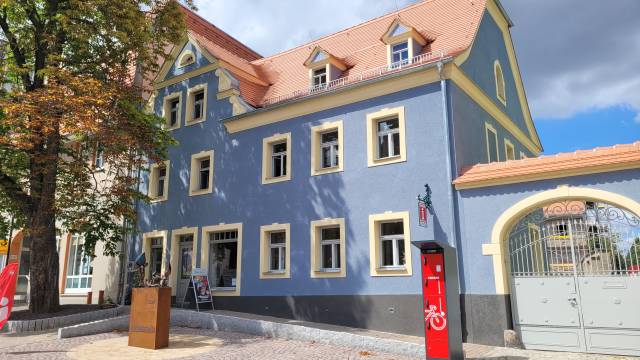 Außenansicht Tourist-Information Bad Lausick in charmantem blauem Gebäude mit Skulptur und Rad-Service – einladender Ort für Gäste mitten in der Stadt.