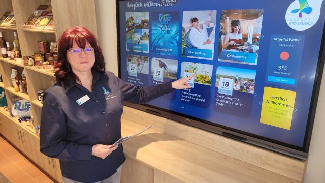 Infoschirm Mitarbeiterin der Tourist-Information Bad Lausick zeigt auf großen Touchscreen mit Infos zu Freizeit, Übernachtung und Veranstaltungen.
